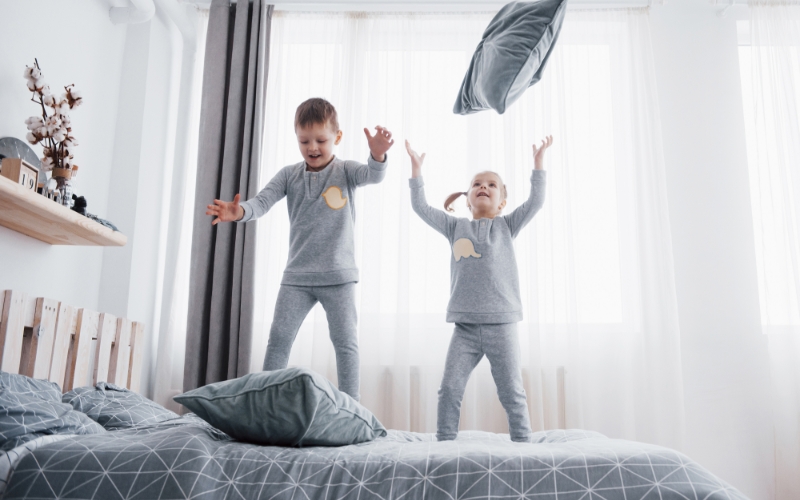 Two children standing on a mattress playing with pillows