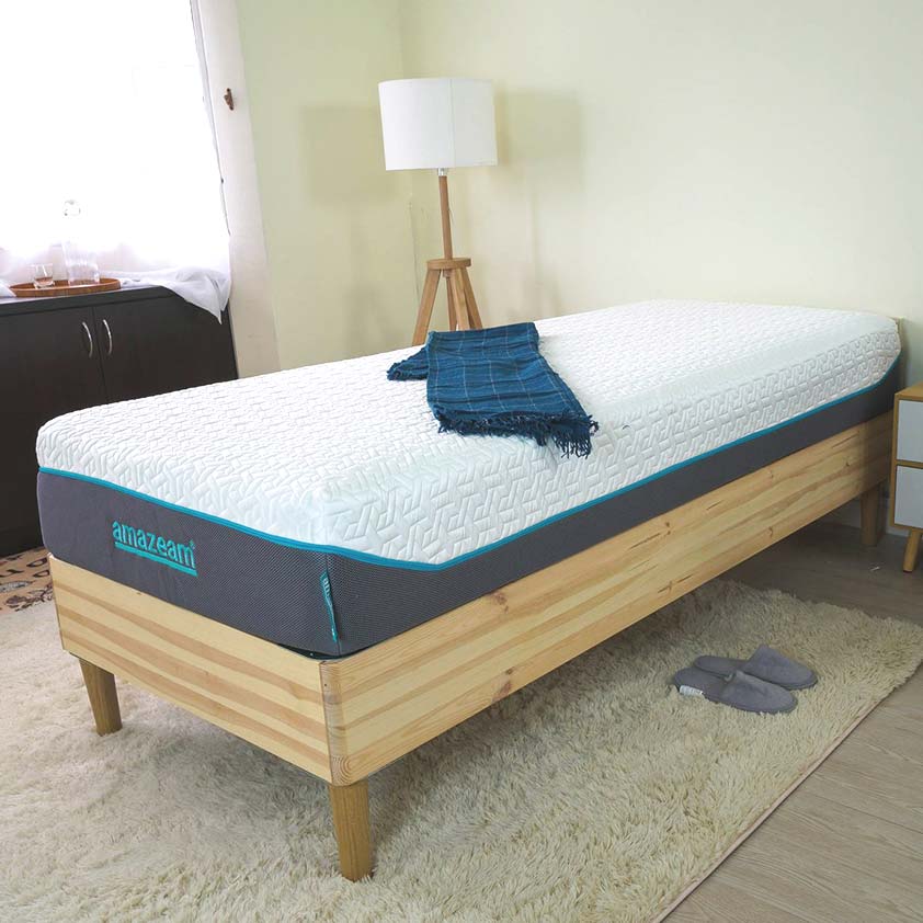 Amazeam Mattress in a bedroom with grey bedroom slippers on the floor and a blue throw on the bed