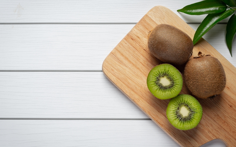 Kiwi fruits on a wooden chopping board on a white table