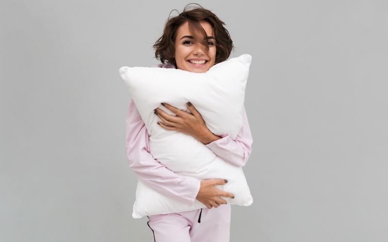Woman with short brown hair in pink pyjamas hugging a pillow